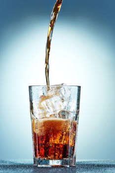 Cola pouring in a glass  with ice on a blue background