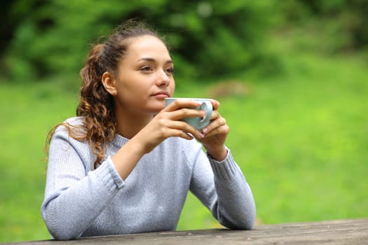 Distracted woman in a park drinking coffee looking away