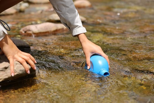 Close up of a hiker hand filling canteen with raw water from river