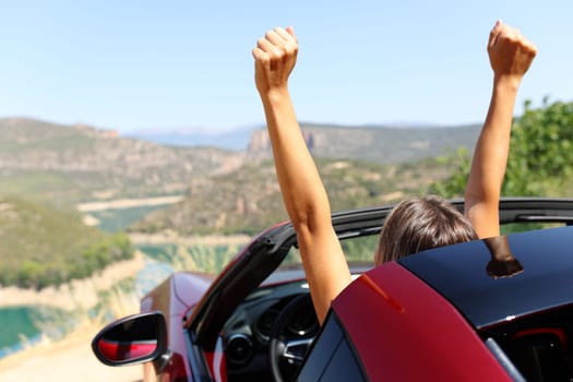 Back view portrait of a happy woman in a convertible car raising arms