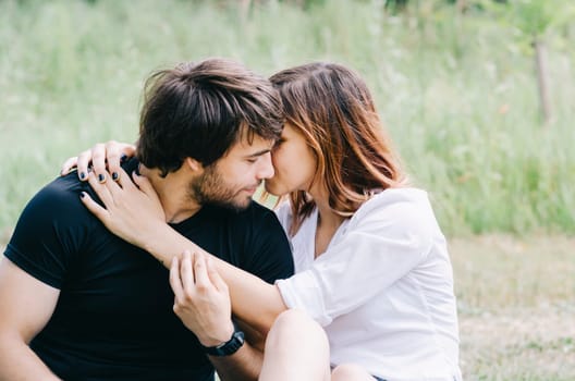 Happy loving couple hugging and kissing in nature. Portrait of young attractive smiling man and woman relaxing in green forest on sunny day.