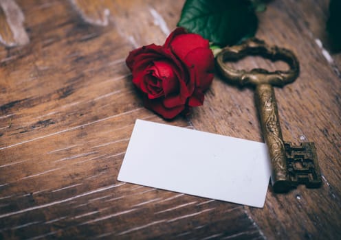 Valentine's day still life concept. Valentine gift, red rose, vintage key and empty greeting card on wooden table. Valentine holiday design.