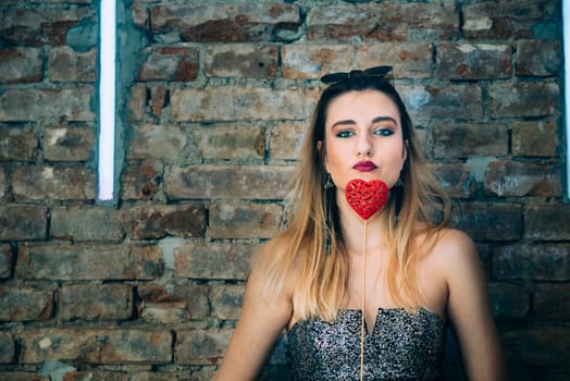 Beautiful stylish young woman holding valentine heart in in nightclub. Valentine's day party.