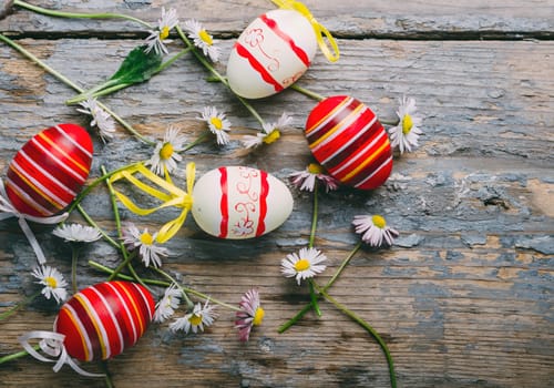 Easter eggs and spring daisy flower on rustic wooden background from above. Top view still life easter concept.