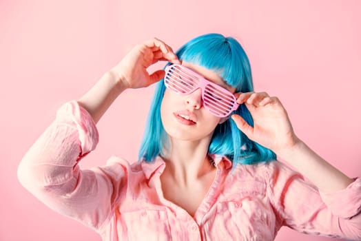 Beautiful young woman with blue color dyed hair with hipster party glasses dancing in front of pastel studio background.