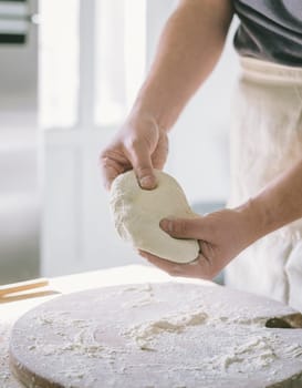 Man kneading dough and baking homemade pastry in the kitchen. Closeup on baker's hands preparing loaf of bread. Cooking and food preparation at home.