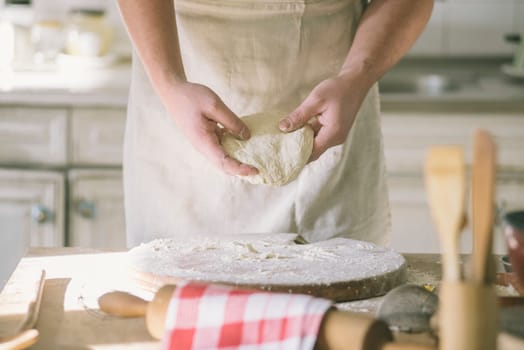 Man kneading and baking homemade pizza dough in the kitchen. Closeup on baker's hands preparing loaf of bread. Cooking and food preparation at home.