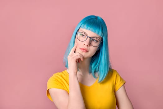 Beautiful pensive young woman with blue color dyed hair with hipster style spectacles thinking in front of pastel studio background.