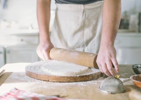 Man rolling and baking homemade dough in the kitchen. Closeup on baker's hands preparing loaf of bread. Cooking and food preparation at home.