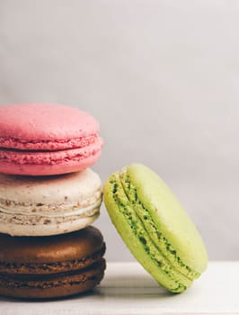 Retro pastel colorful macaroons pile on vintage background. Homemade french macaron dessert candy with different flavors: chocolate, strawberry, vanilla, pistachio.