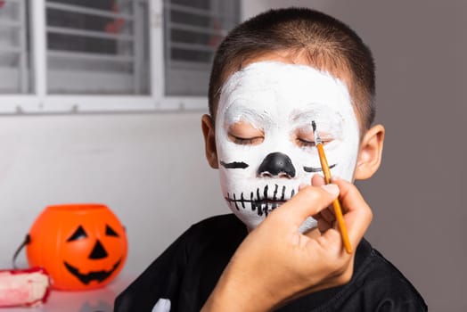 Portrait of woman applying color brush to child face for party at home, family Asian mother and kid son getting makeup halloween face painting look like ghost, Happy halloween day concept