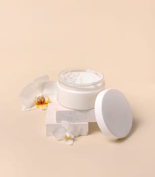 Opened Cream jar with a blank white lid near white orchid flowers on light yellow close up. Cosmetic packaging Mockup. Exotic natural cosmetics, romantic composition, everyday skincare routine..