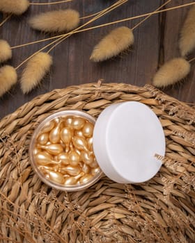 Beauty serum capsules in an opened jar with blank lid on wattled boho placemat near Hare's Tail grass top view. Skincare product for everyday beauty routine. Bohemian eco friendly cosmetics