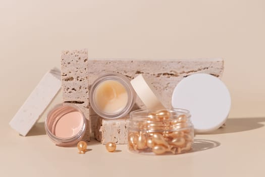 Opened cream jars on travertine stones on light beige close up, mockup. Skincare beauty product package. Exotic natural cosmetics, pastel minimal composition..