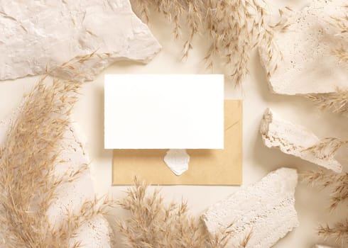 Blank card and enveelope near beige travertine stones and dried pampas grass top view, mockup. Boho scene with horizontal card. Bohemian or close to nature greeting or wedding Invitation.