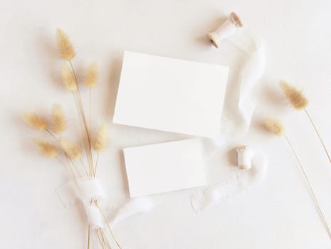 Blank cards near silk ribbons and dried hare's tail grass top view on white, mockup. Boho romantic scene with horizontal cards. Bohemian or close to nature greeting or wedding Invitation