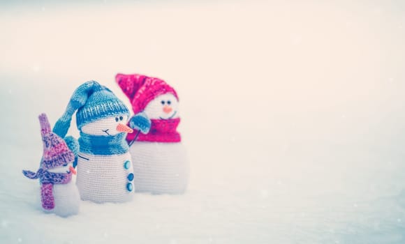 Little knitted snowmen on the white snow in nature. Concept of the wallpaper and greeting card.