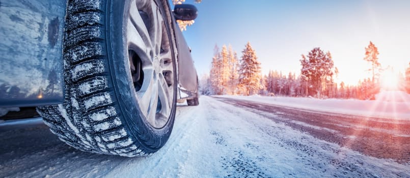Closeup view of the car's wheel on the snowy road in natural park. Beautiful panoramic view.