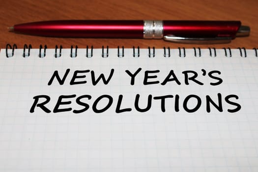 Notepad with a pen on a wooden table. View from above. The concept of resolutions for the new year.