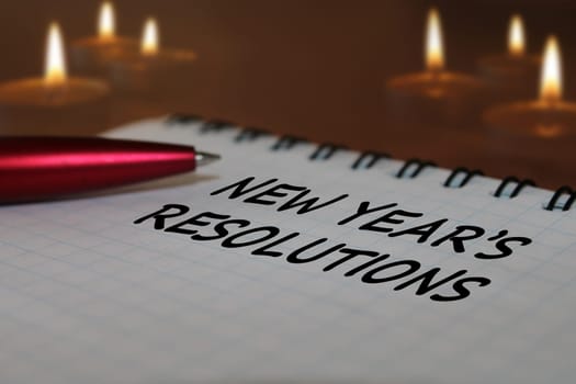 Notebook with a pen on a wooden table against the background of burning candles. The concept of resolutions for the new year.