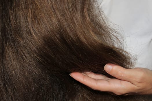 A girl with long dark hair holds curls in her hand. Hair care. Hair loss problem.
