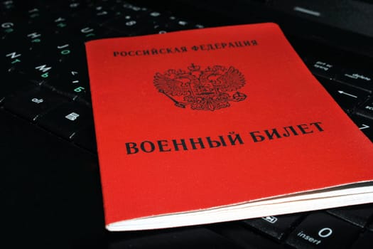 A military ID issued by the Russian Federation lies on a computer keyboard close-up. The concept of mobilization.