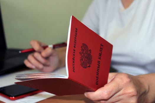 The girl holds a military ID issued by the Russian Federation in her hand and writes down his data. The concept of mobilization.