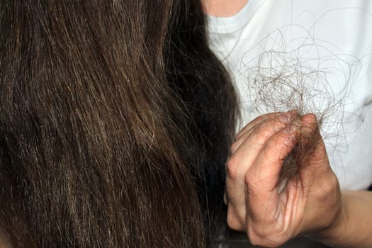 A girl with long dark hair holds a bunch of fallen hair in her hand. Hair loss problem.