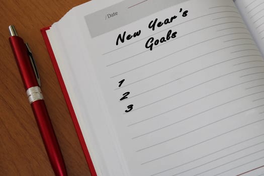 Notepad with a pen on a wooden table. View from above. The concept of goals for the new year.