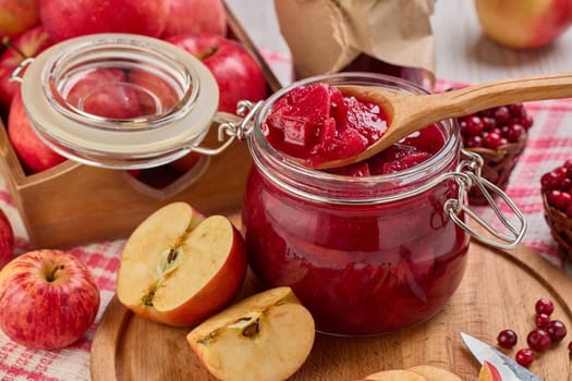 Wooden spoon with appetizing lingonberry and apple jam, jar of jam, fresh fruits and berries on light wooden table. Autumn harvest,  Home canning. Top view. Closeup