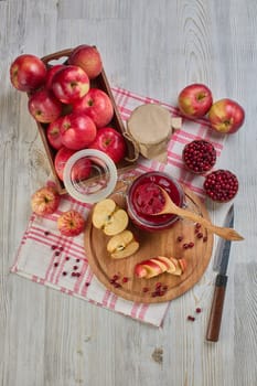 Wooden spoon with appetizing lingonberry and apple jam, jar of jam, fresh fruits and berries on light wooden table. Autumn harvest,  Home canning. Top view.