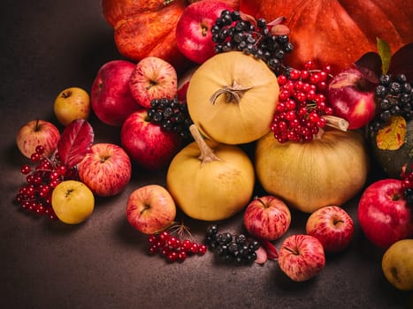 Thanksgiving background. Festive still life with pumpkins, berries, autumn leaves and apples on dark brown background. Happy Thanksgiving  day, autumn harvest, Halloween. Top view