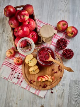 Wooden spoon with appetizing lingonberry and apple jam, jar of jam, fresh fruits and berries on light wooden table. Autumn harvest,  Home canning. Top view.