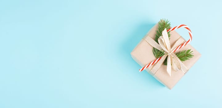 Christmas holiday greeting card with little gift box, candy cane, ribbon and fir branches, blue background