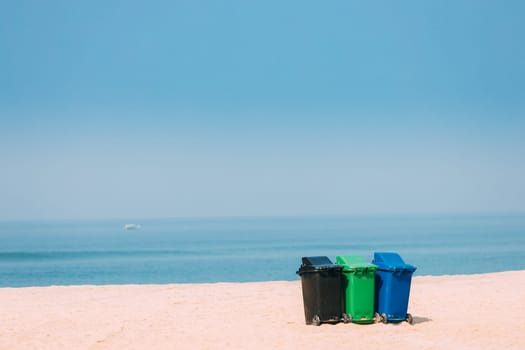 Three Colorful Plastic Waste Containers On Wheels For Separate Collection Of Garbage. Containers For Temporarily Storing Waste. Dustbins, Garbage Cans, Trash Cans On Sea Ocean Coast Beach.