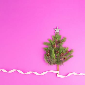 Christmas tree made from fir branches, pine cones and a cinnamon stick as the trunk, pink greeting card with copy space