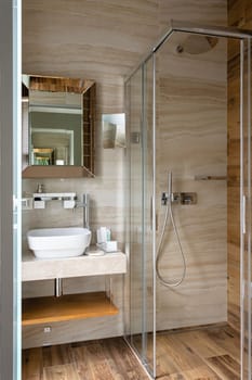 Stylish modern bathroom with glass walk-in shower in new luxury home. Spacious and bright modern bathroom interior with light and brown walls, shower, white washbasin and stylish mirror.