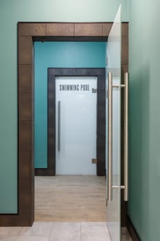 Closed stylish front door with inscription swimming pool in English. Corridor of stylish modern new public space with doors leading to has swimming pool.
