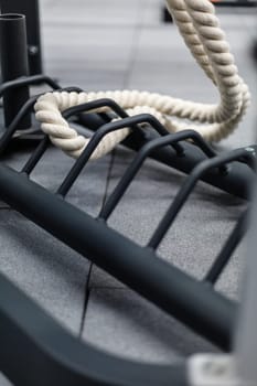 Sport and fitness equipment. Close up of fitness battle rope attached to black metal grille in fitness gym. White training rope is located in sports complex with gray floor.