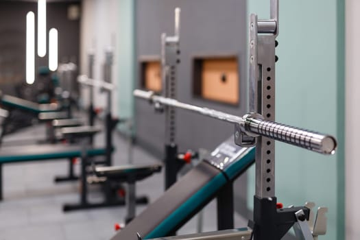 Vertical weight lifting equipment. Close up of empty barbell bar without plates on rack in gym club. High quality equipment and gym maintenance. Selective focus. Sports background.