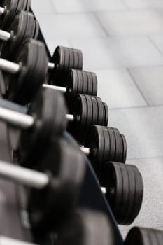 Sport equipment and tool theme. Close up of gym equipment, black metal dumbbells lying in row on rack in modern sports complex. Sport concept. Selective focus.