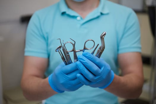 Professional dentist uses special sterilized medical instruments in modern dental clinic. Male doctor in blue latex gloves demonstrates set of metal dental tools.