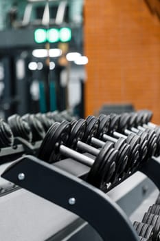 Close up set of dumbbells on black metal steel on rack in sports fitness center. Dumbbells in row are ready for use by athletes. Workout training and fitness gym concept.