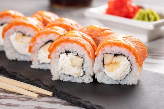 Popular food. Set of Philadelphia sushi on black concrete plate on table. Close up of pieces of sushi rolls with salmon on top and with cheese and eel inside.