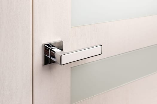 Close up of beautiful and stylish new metal door knob on modern interior door. Silver door handle with white insert on light beige door with frosted glass.