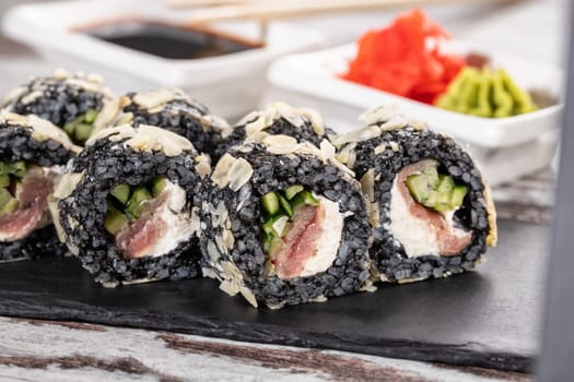 Close up of original unconventional sushi with black rice. Close up of pieces of sushi roll on black metal board.