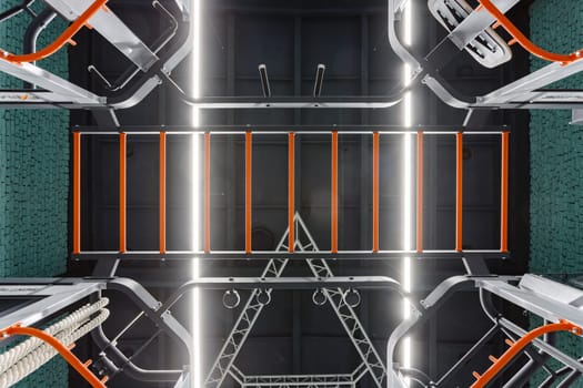 Sports background. Stylish modern interior gym with details from sports equipment. Bottom view of sports equipment bars and exercise machines in black and orange in sports complex with modern lighting