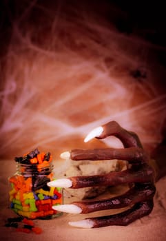 Halloween concept with witch hand and colorful candy in a glass jar