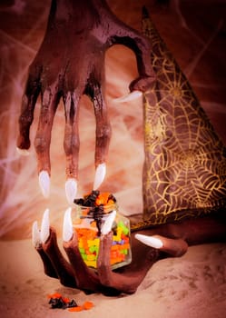 Pinhole effect Halloween witch hands and colorful candy in a glass jar