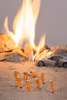 Miniature firefighters practicing safety fire drill at a car accident scene in flames